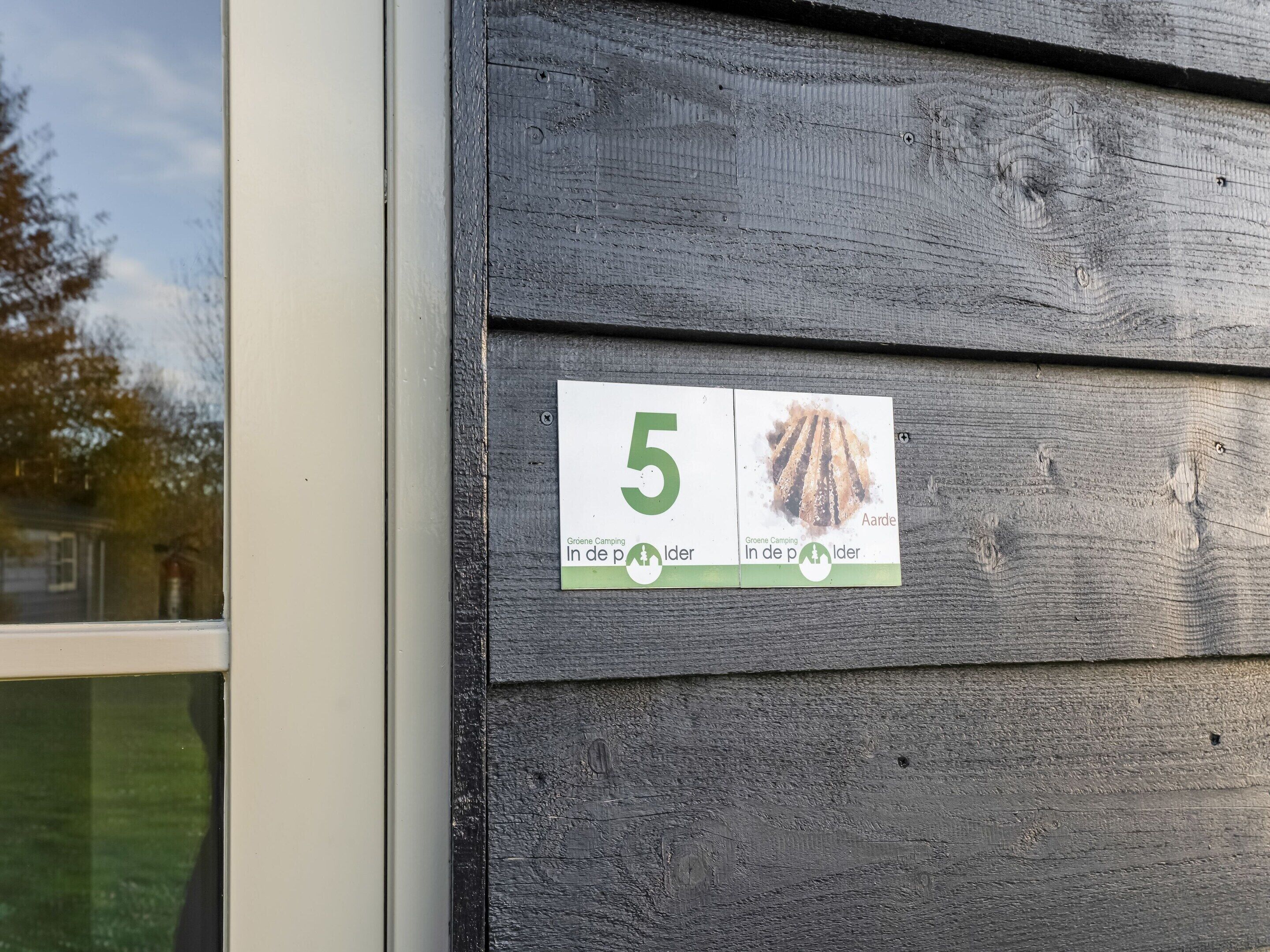 En træfacade med et hvidt skilt, der viser nummer 5 samt to billeder af en seng og et træ.
