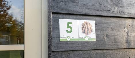 En træfacade med et hvidt skilt, der viser nummer 5 samt to billeder af en seng og et træ.