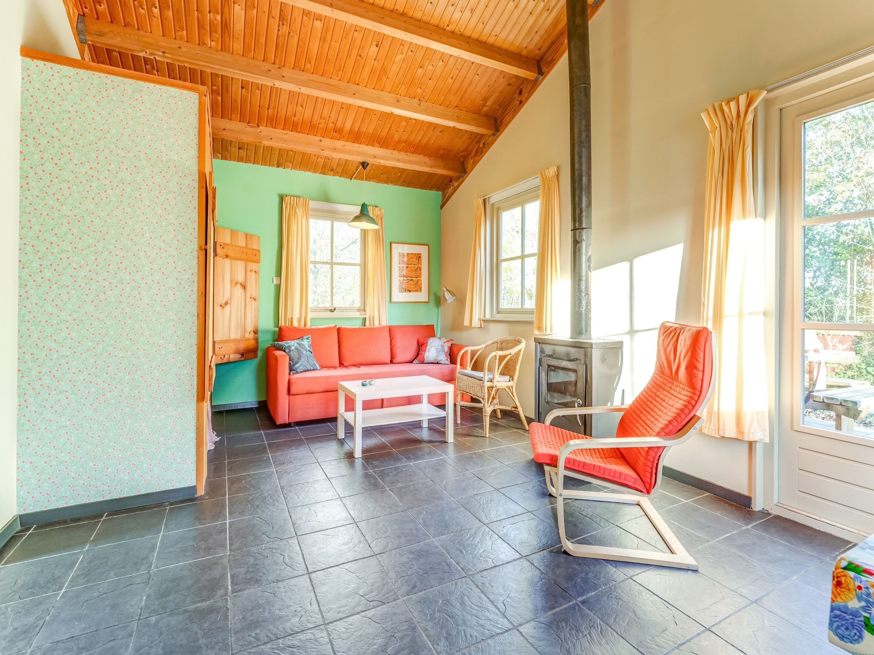 Una sala de estar acogedora con techo de madera, un sofá rojo, una mesa blanca y una mecedora.