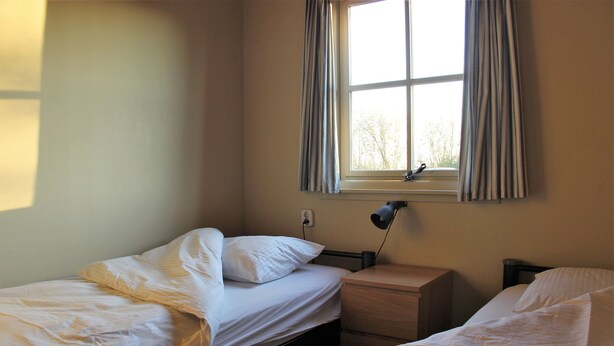 Een kamer met twee bedden, een nachtkastje, een lamp en een raam met gordijnen.