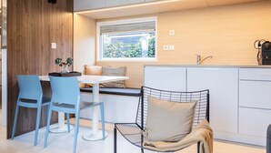 Une cuisine moderne avec des meubles blancs, un coin repas avec des chaises bleues et une fenêtre donnant sur un paysage verdoyant.