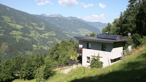 A modern house with solar panels on the roof, surrounded by lush green hills and mountains. - Apartment in Aschau Near Kaltenbach Ski Lift (Aschau Im Zillertal)