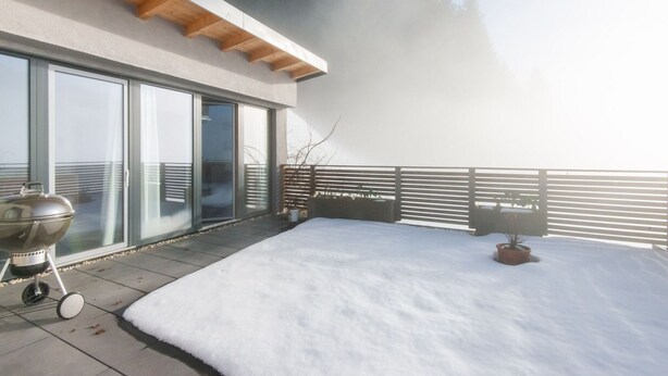 A modern outdoor patio with a snow-covered floor, a barbecue grill, and a view of a forested area. - Apartment in Aschau Near Kaltenbach Ski Lift (Aschau Im Zillertal)