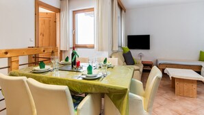 A dining area with a table set for four, a sofa, a bench, and a TV mounted on the wall. - Apartment in Aschau Near Kaltenbach Ski Lift (Aschau Im Zillertal)