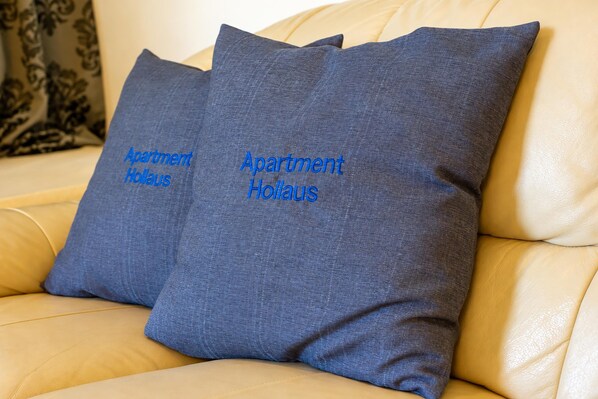 Dos almohadas con el texto 'Apartment Hollaus' sobre un sofá color beige.