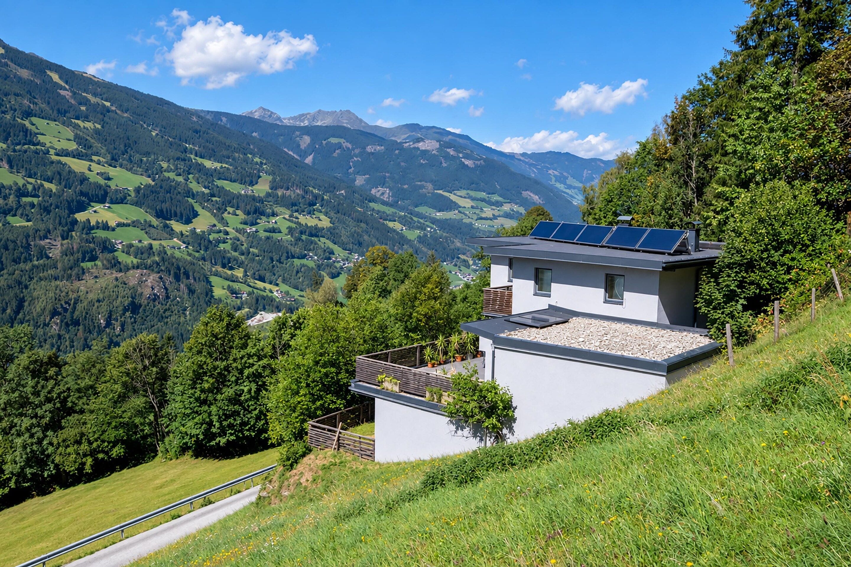 Une maison moderne dotée de panneaux solaires sur le toit, entourée d’une végétation luxuriante et de montagnes.
