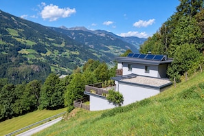 Ein modernes Haus mit Solaranlage auf dem Dach, umgeben von üppiger Vegetation und Bergen.