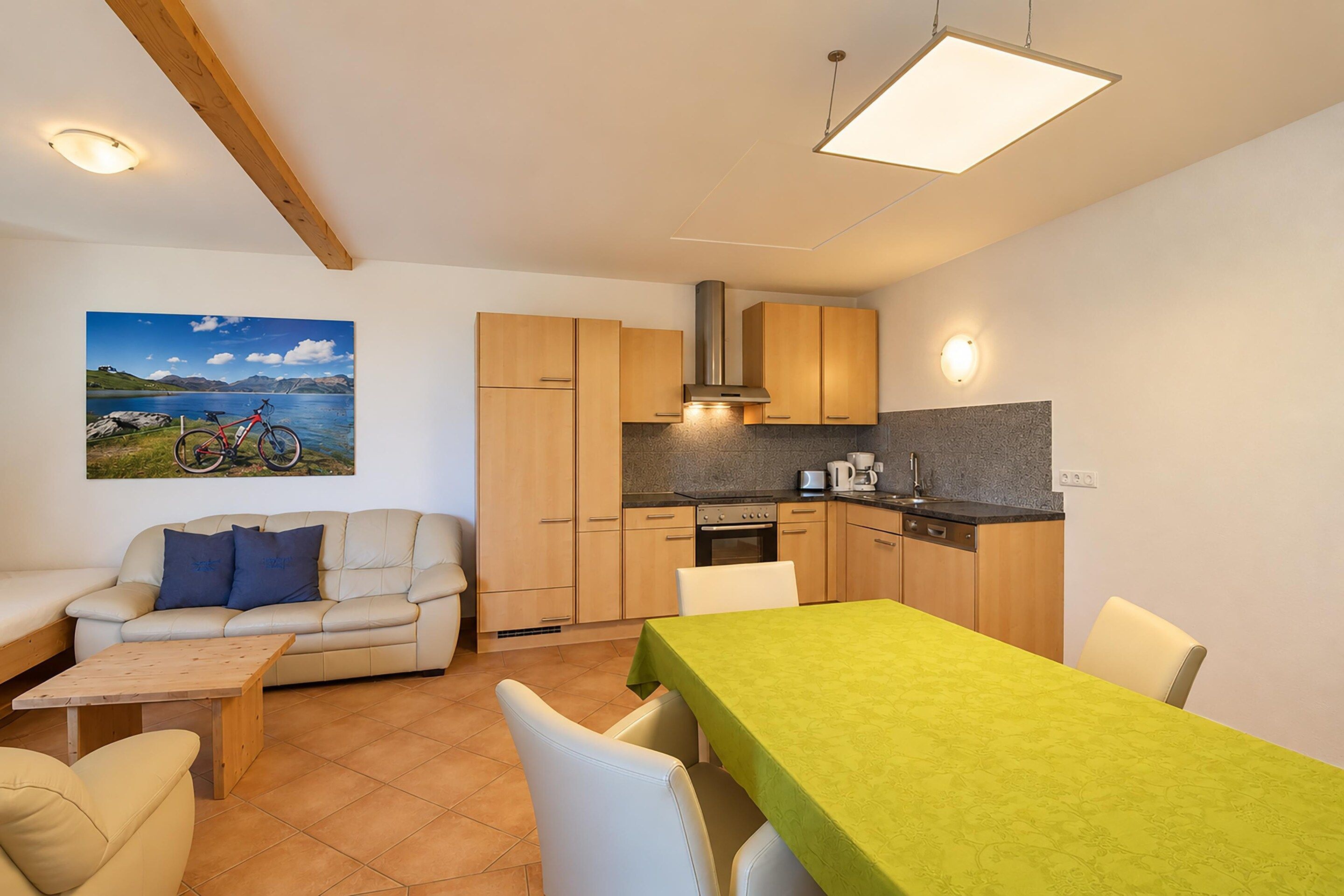 Un espace de vie compact comprenant un canapé, une table à manger, un coin cuisine et un tableau accroché au mur.