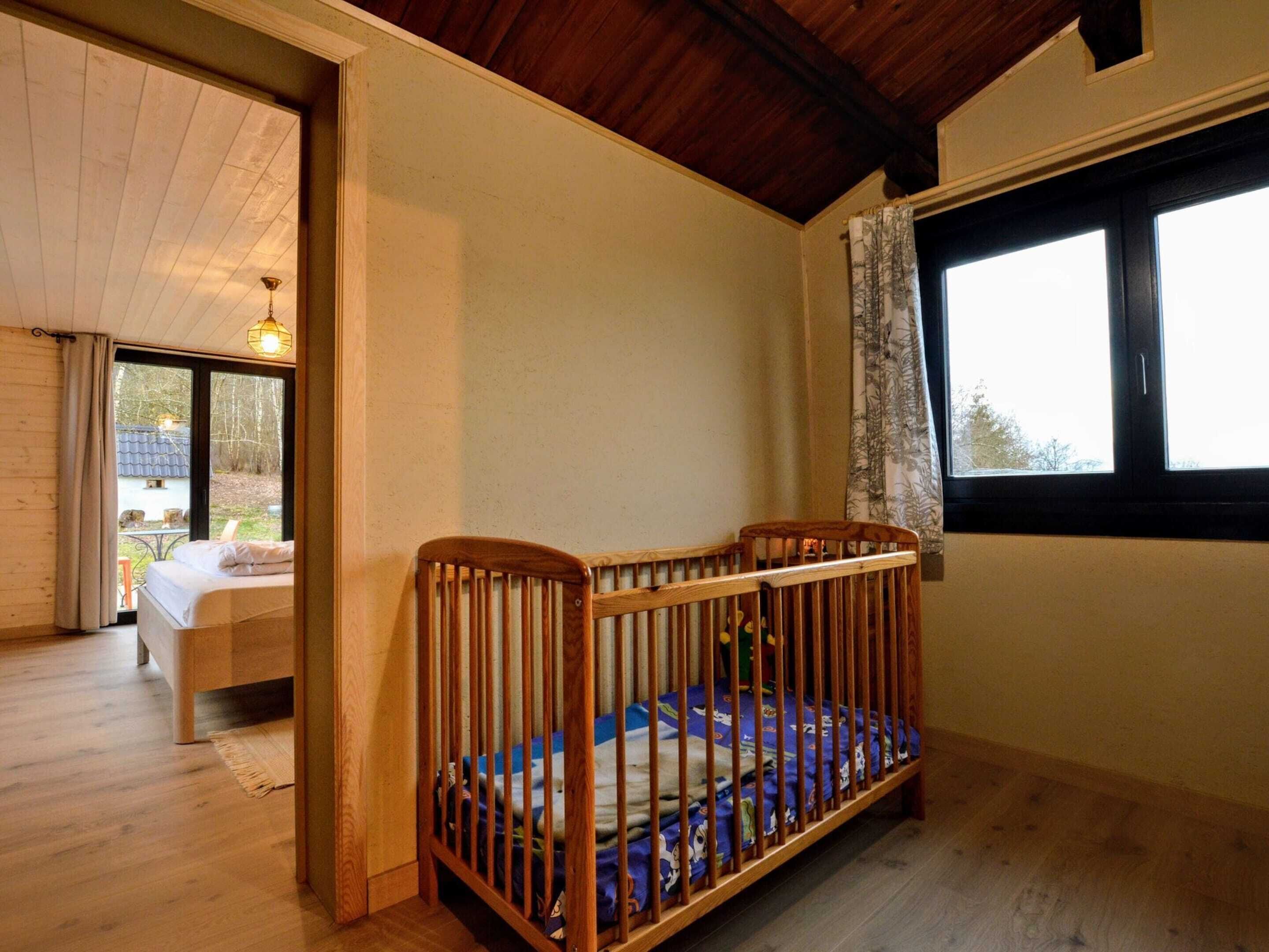 A room with a wooden crib, a bed, and a window with curtains.