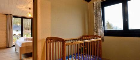 A room with a wooden crib, a bed, and a window with curtains.
