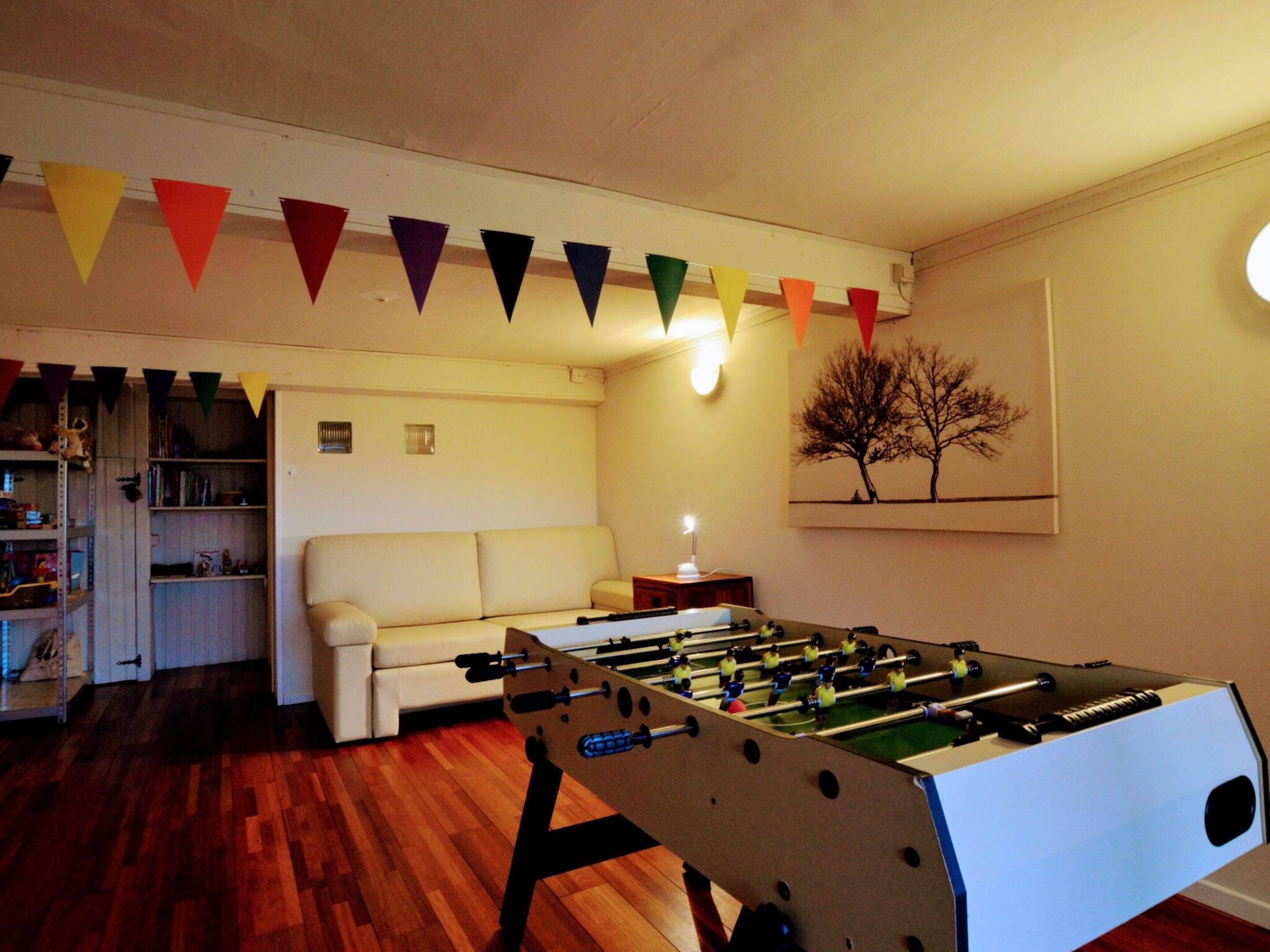 A cozy living room with a foosball table, a white sofa, a bookshelf, and a wall-mounted painting.