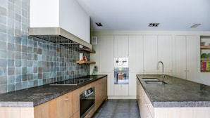 Een moderne keuken met een zwart aanrecht, houten kastjes, een inbouwoven en een roestvrijstalen koelkast.