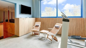 Een moderne spa-ruimte met twee ligbedden van hout, een groot raam met uitzicht op bomen, en een flatscreen televisie aan de muur.