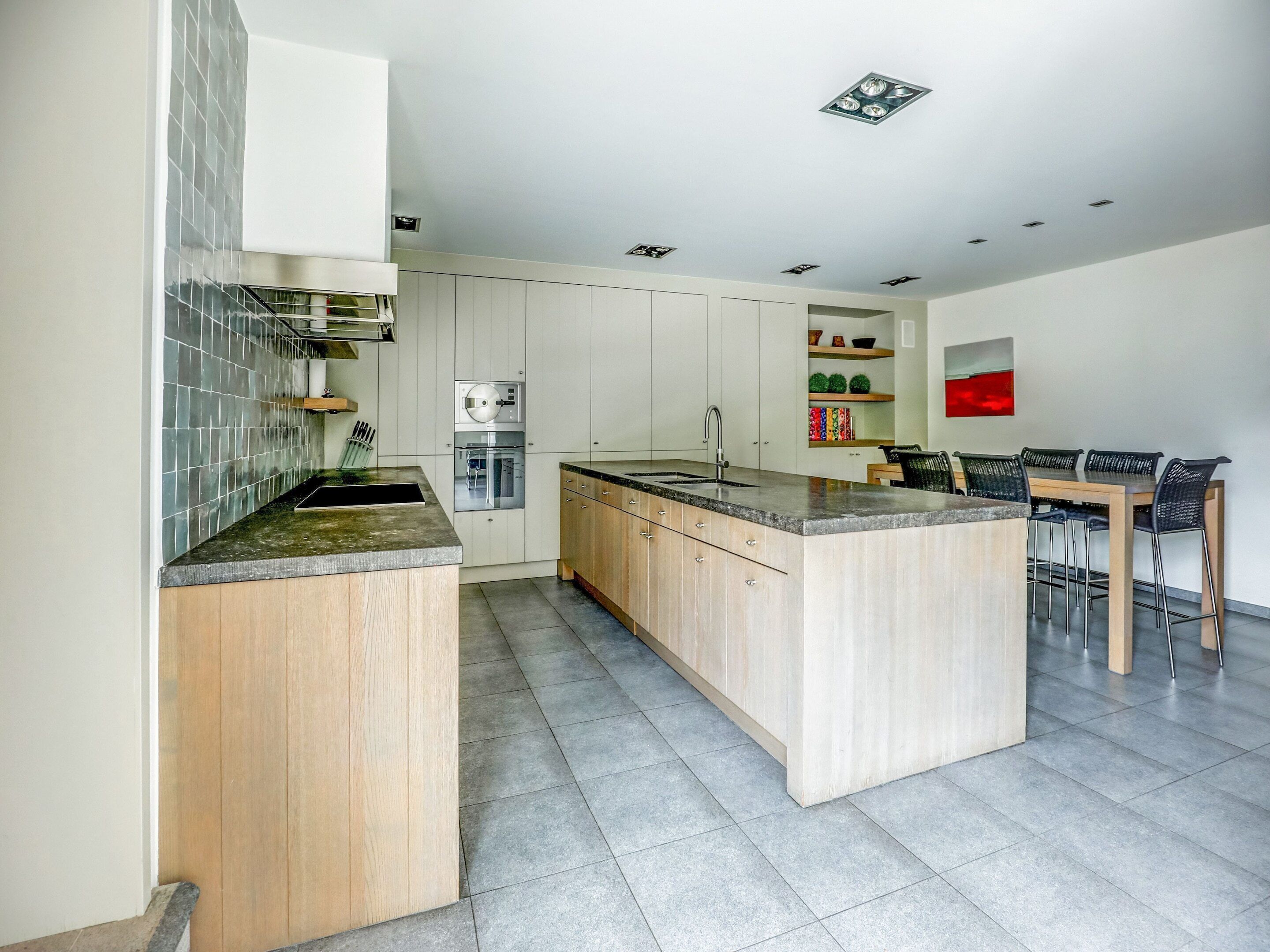 A modern kitchen with a central island, a dining area with a table and chairs, and built-in appliances.