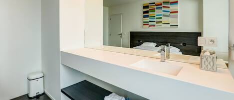 A modern bathroom with a white vanity, a large mirror, a dark headboard, and a towel rack with folded towels.