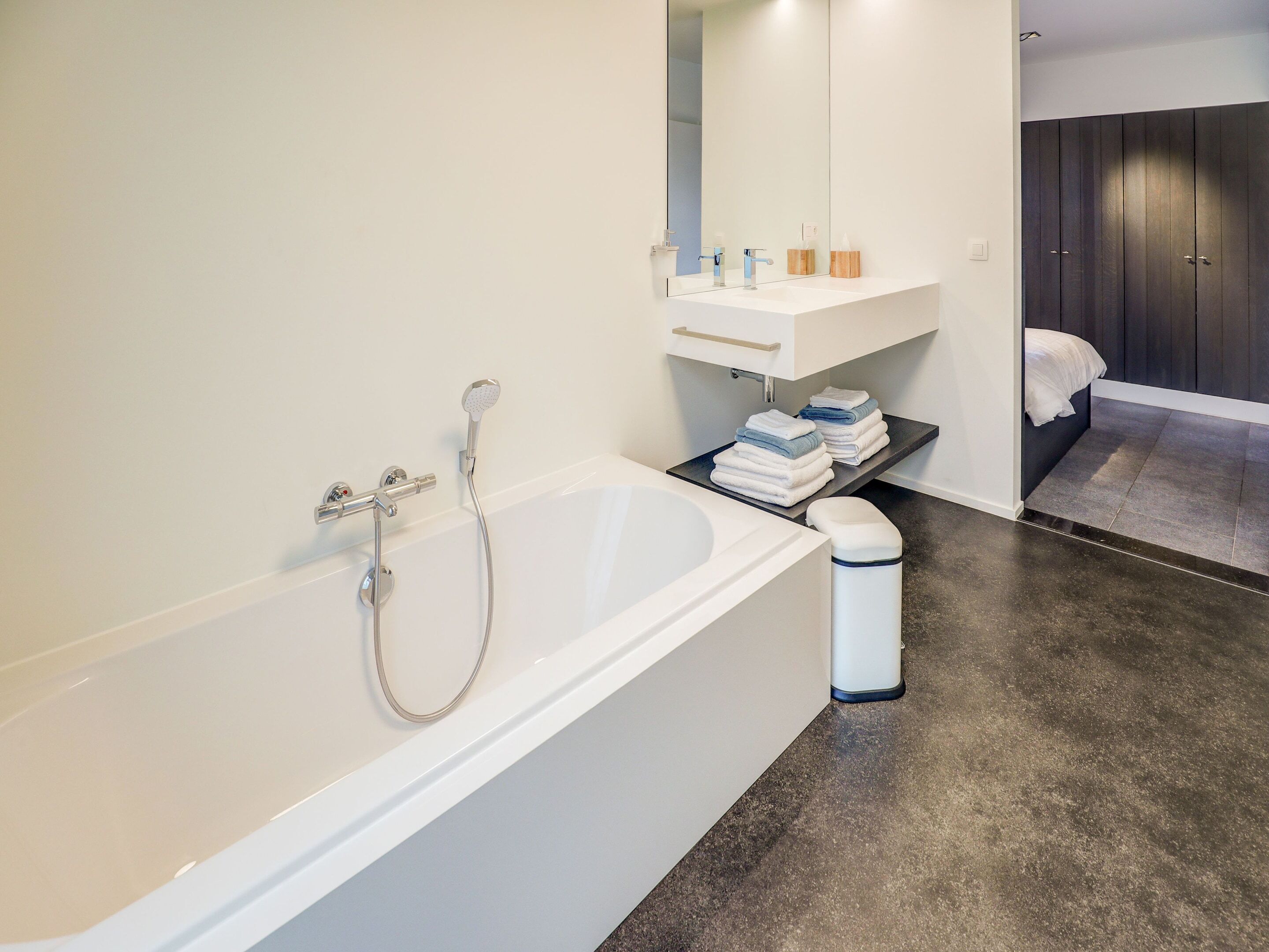 Un bagno moderno con vasca, lavabo e specchio. Si nota uno scaffale con asciugamani e articoli da toilette.