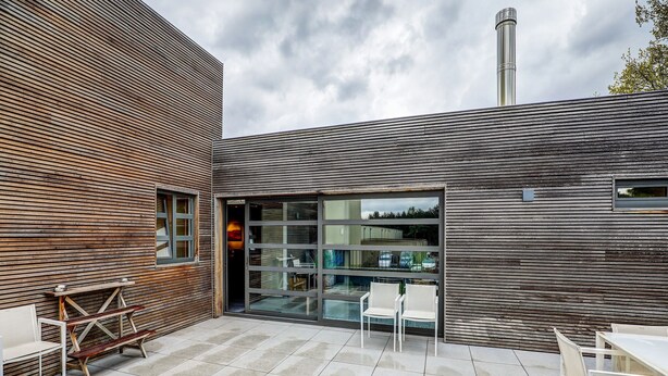 Een modern gebouw met een houten gevel, een glazen deuropening en een patio met terrasmeubilair.