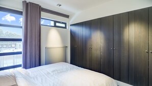 Een slaapkamer met een bed, een raam met gordijnen, een radiator en een kledingkast.