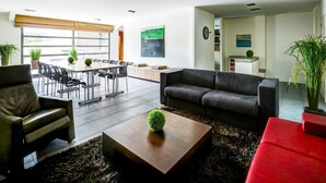 Een moderne woonkamer met een eethoek, een bank, een salontafel en een rode poef.