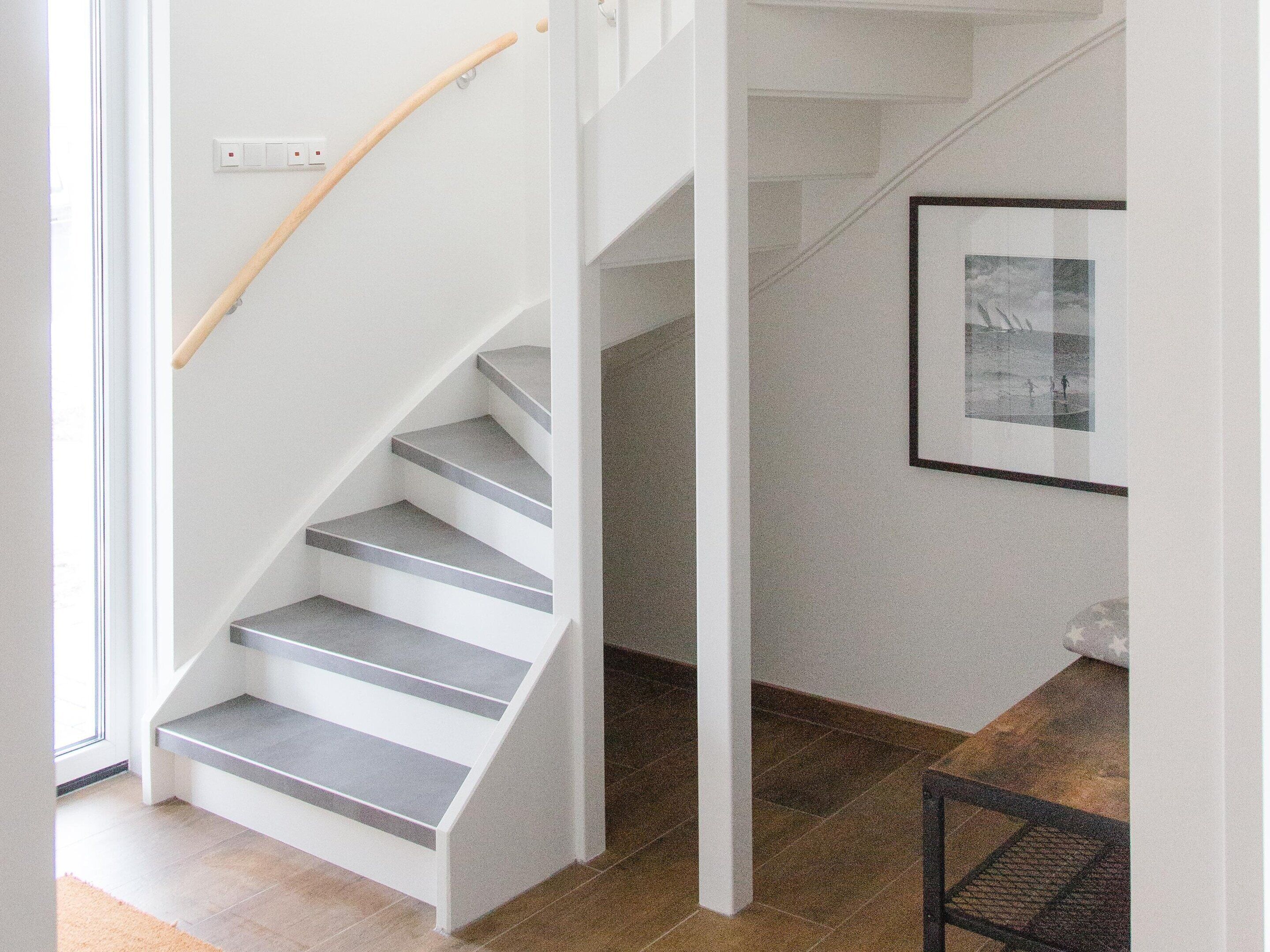 A staircase with grey steps and a wooden handrail, leading to a landing with a framed picture on the wall.