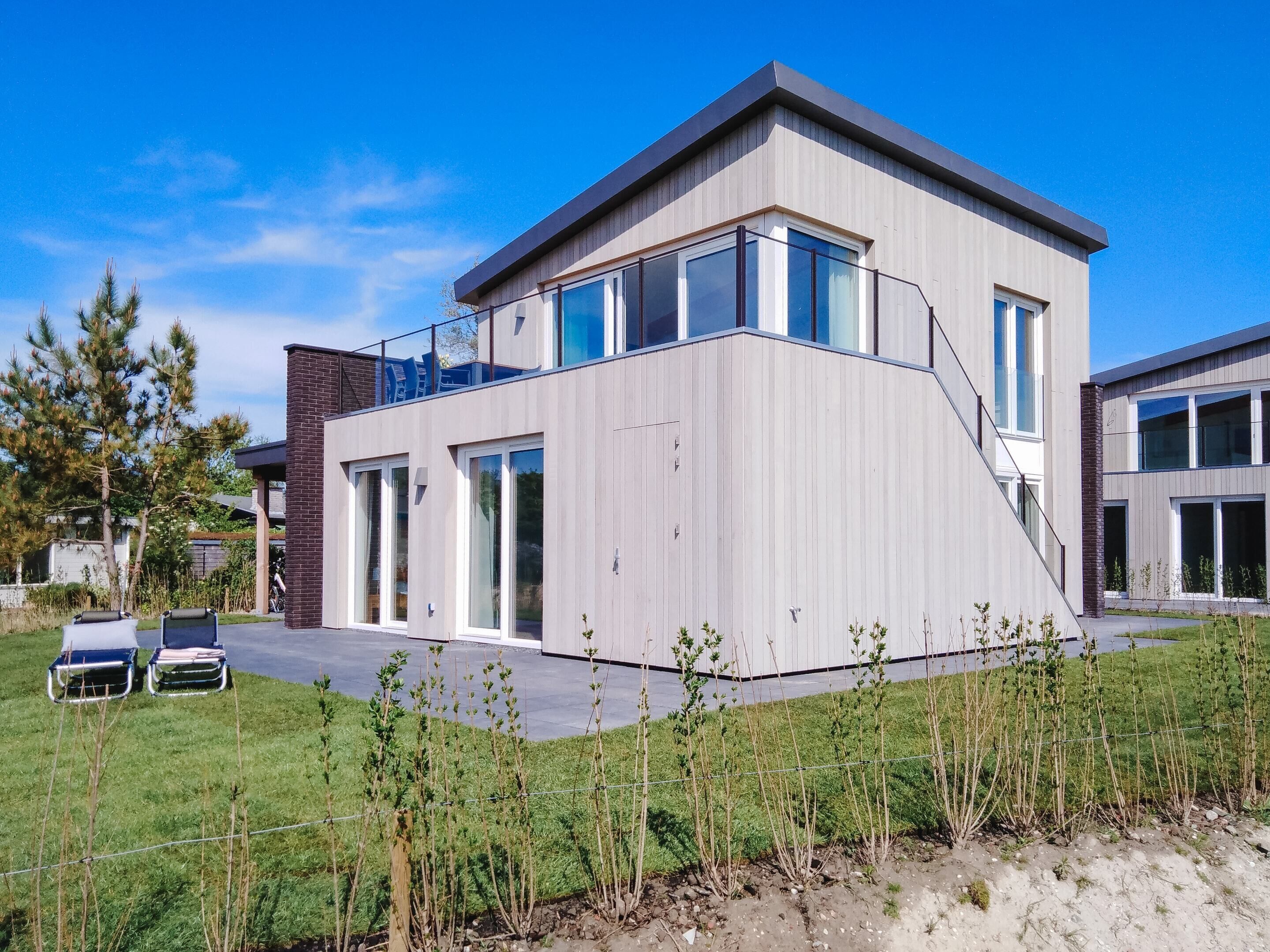 Een modern huis met twee verdiepingen, grote ramen, een plat dak en een klein balkon.