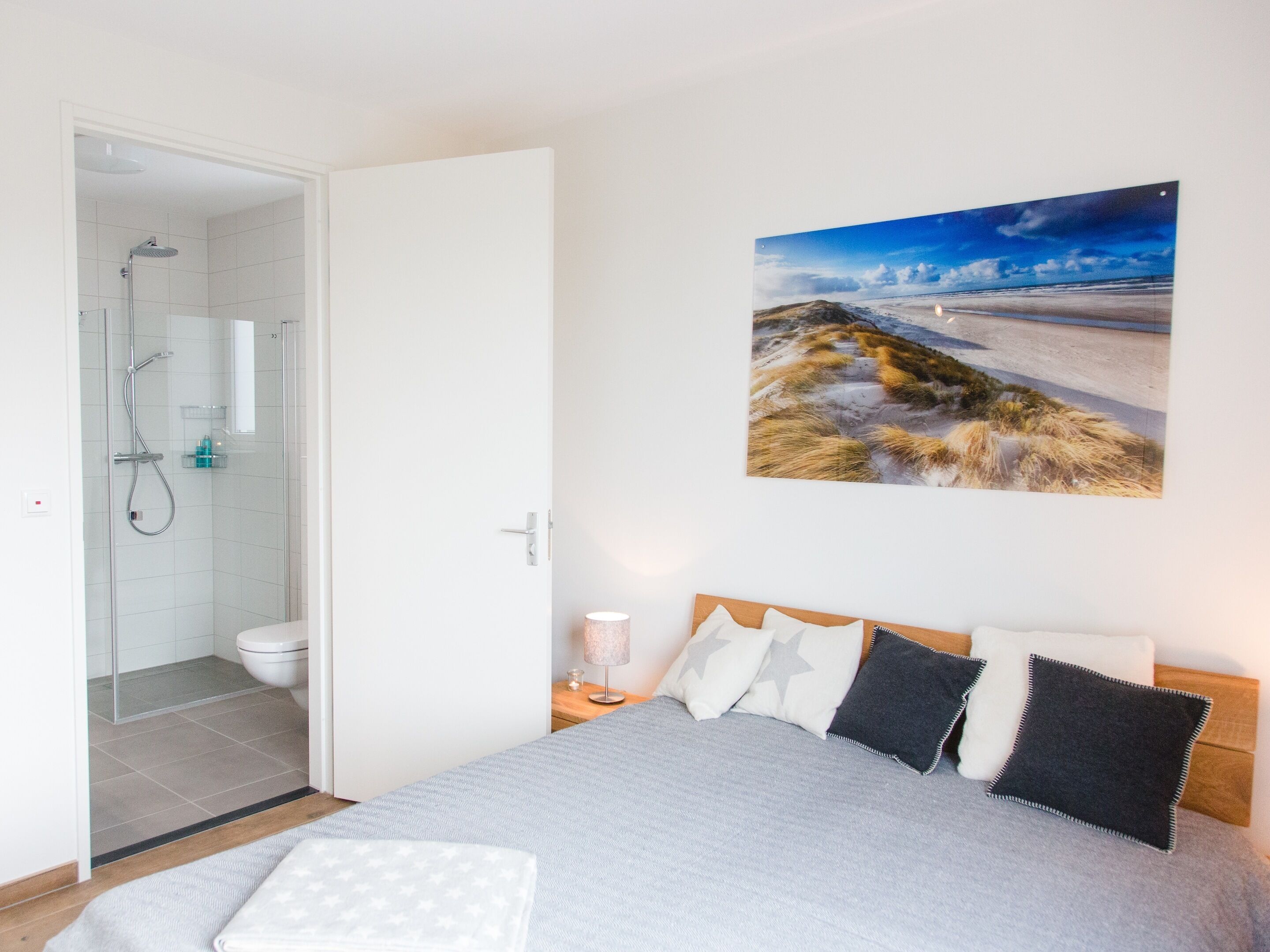 Une chambre à coucher comprenant un lit, une table de chevet, un tableau accroché au mur, et une salle de bain avec douche et toilettes.