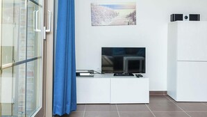 Un salon moderne avec un téléviseur à écran plat posé sur un meuble blanc, un tableau accroché au mur et un rideau bleu.