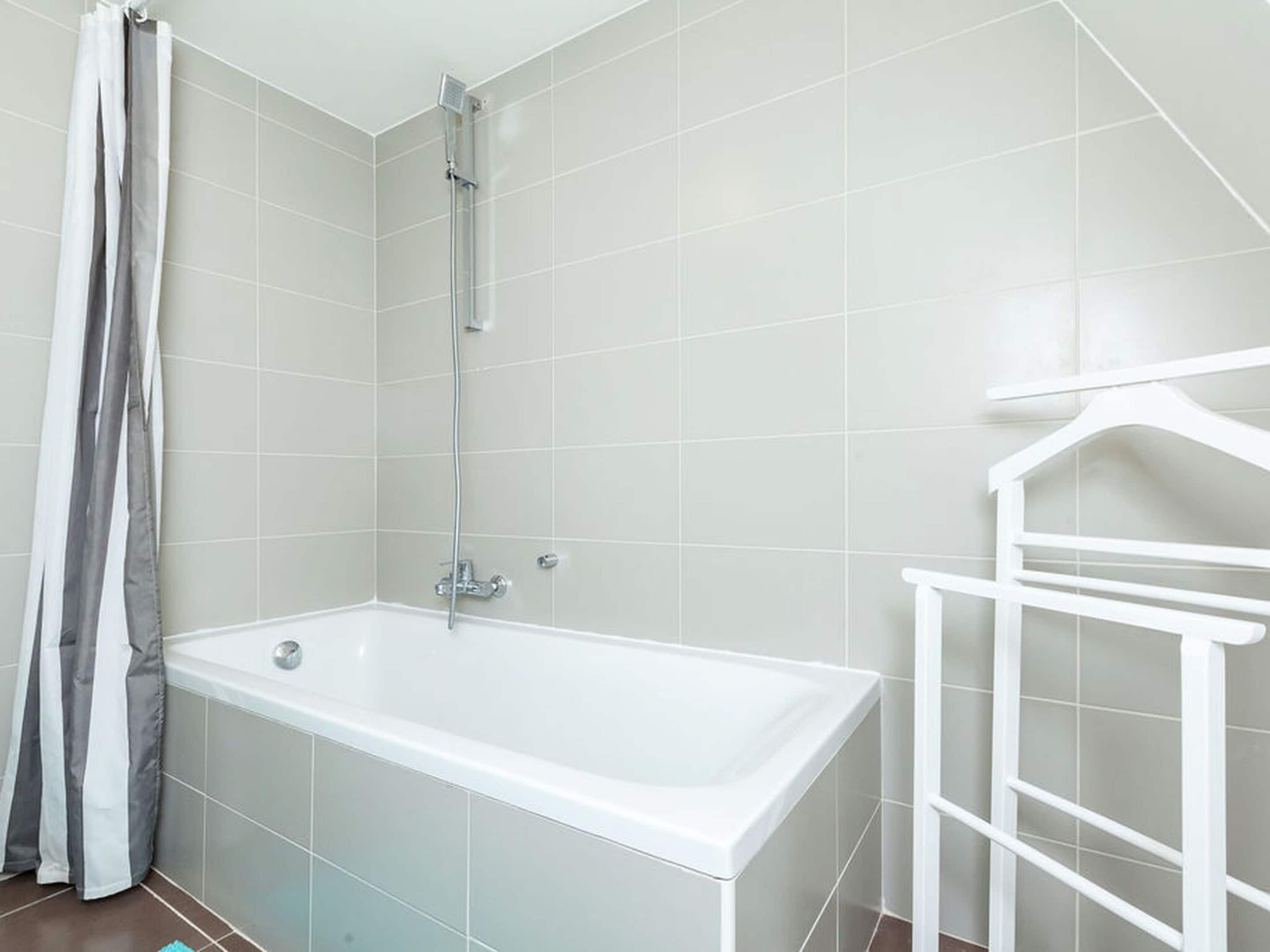 Un baño con una bañera blanca, una ducha y un toallero blanco.