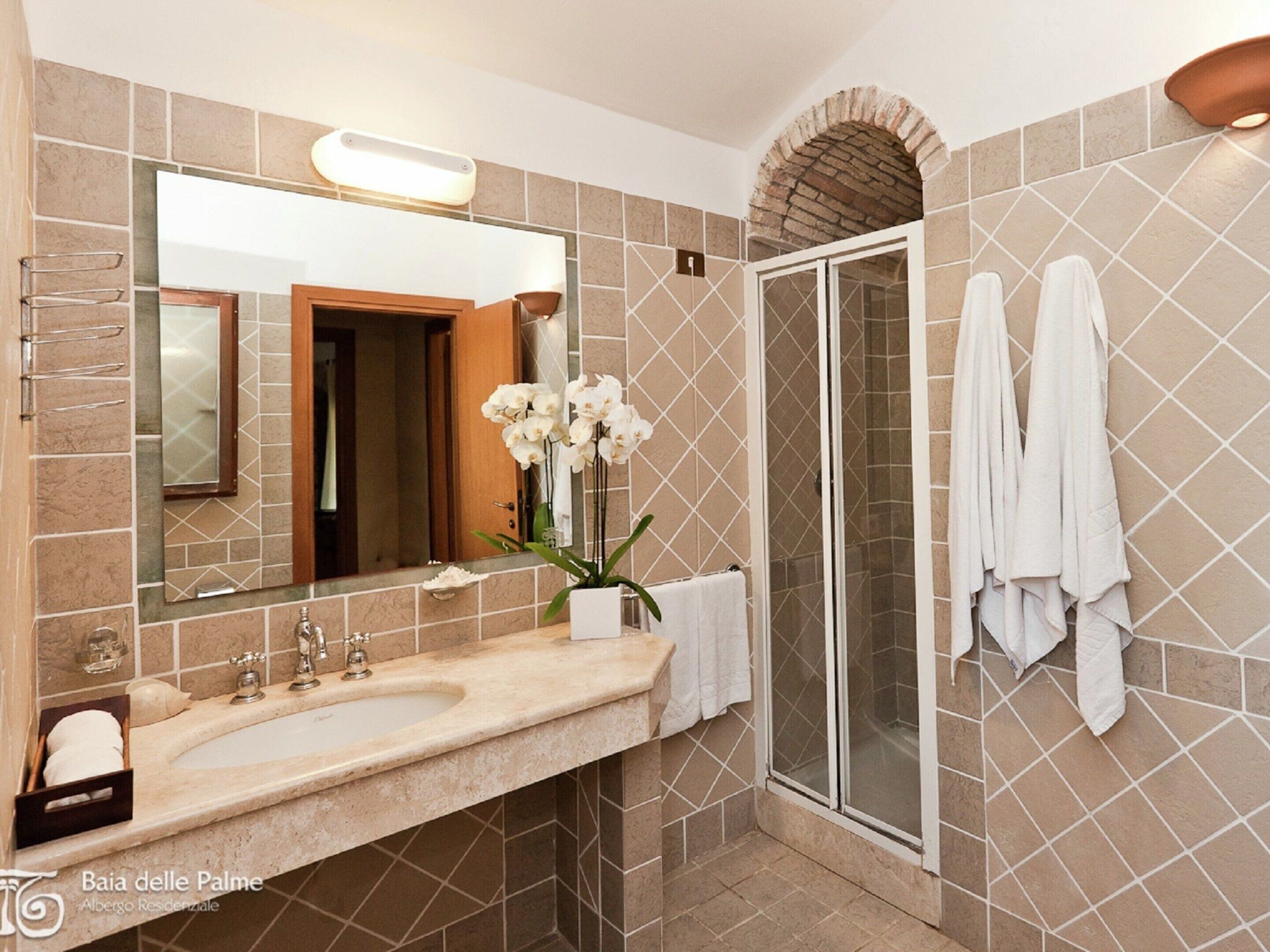 A bathroom with a large mirror, a sink, a shower, and towels hanging on the wall.
