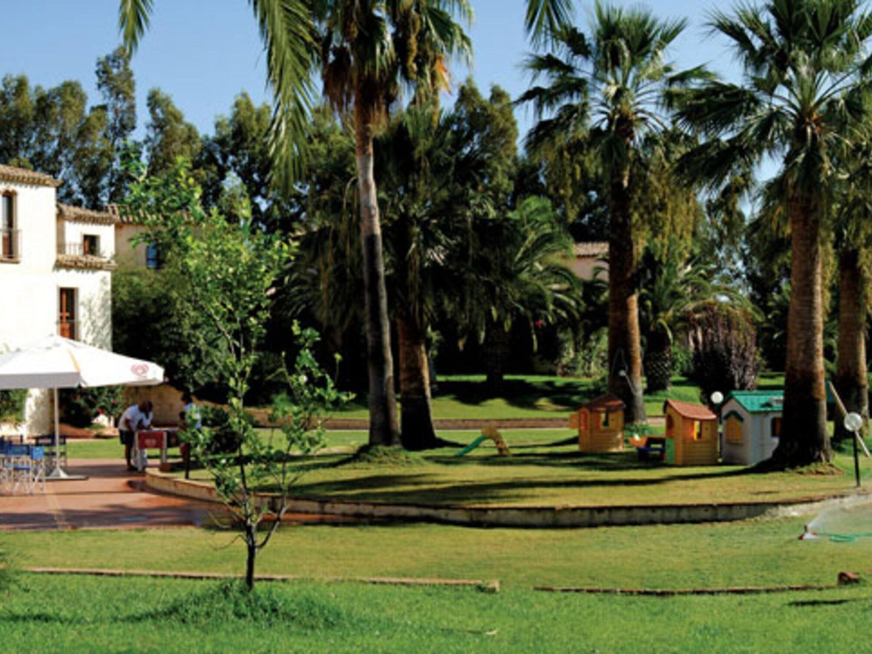 A building with a white facade and a tiled roof, surrounded by palm trees and a well-maintained lawn.