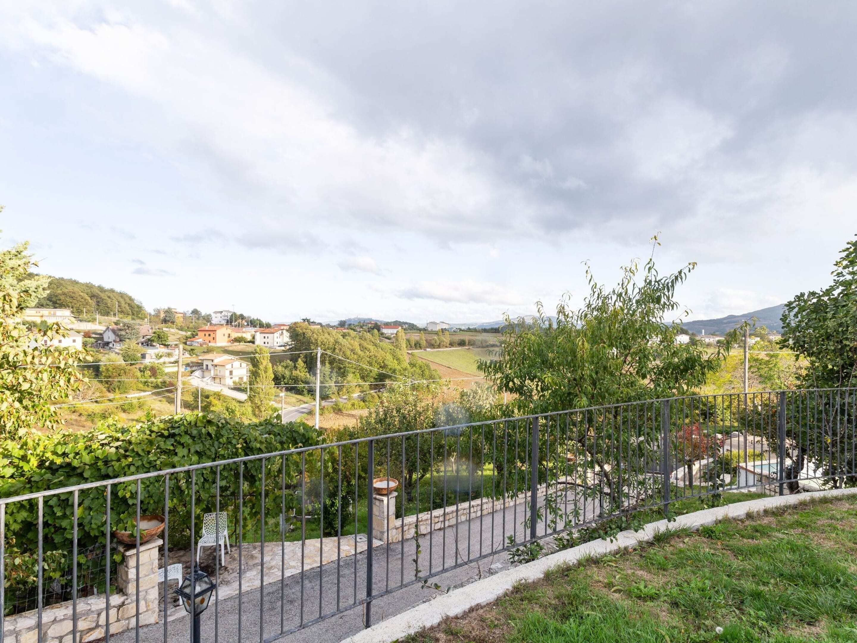 A fenced outdoor area with a bench and a table, overlooking a residential area with houses and greenery.