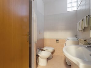 A bathroom with a wooden door, two toilets, a sink, and a bathtub.