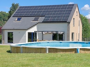 Et moderne hus med swimmingpool, solpaneler og en overdækket terrasse.