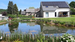 Een huis met een dak voorzien van zonnepanelen, een vijver en een omheind gazon.