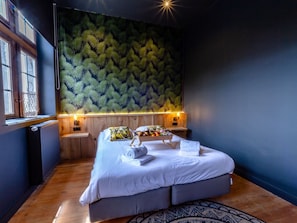 A bedroom with a bed, a window, a wall with a leaf pattern, and a nightstand with a lamp. - Nice Cottage in a Castle-farm in Ohey With Swimming Pond (Ohey)