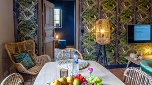 A dining area with a table set for two, surrounded by wicker chairs, a woven placemat, and a fruit arrangement. A television is mounted on the wall, and a lamp is placed on the floor. - Nice Cottage in a Castle-farm in Ohey With Swimming Pond (Ohey)