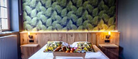 A hotel room with a bed, two nightstands, a tray of breakfast items, and a fern-patterned wall.
