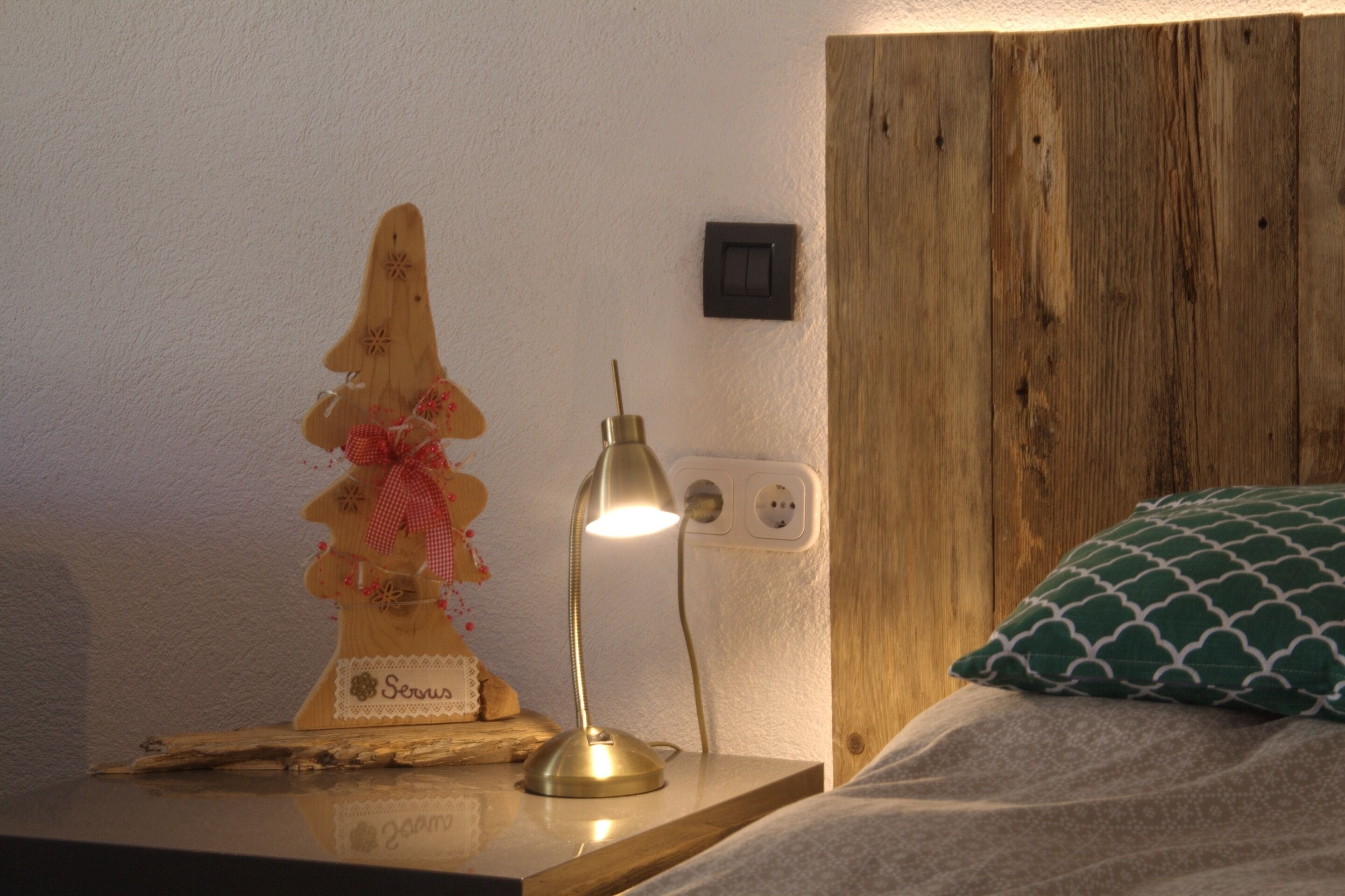 Cabecera de madera, lámpara de noche, una figura decorativa de madera y un cojín estampado.