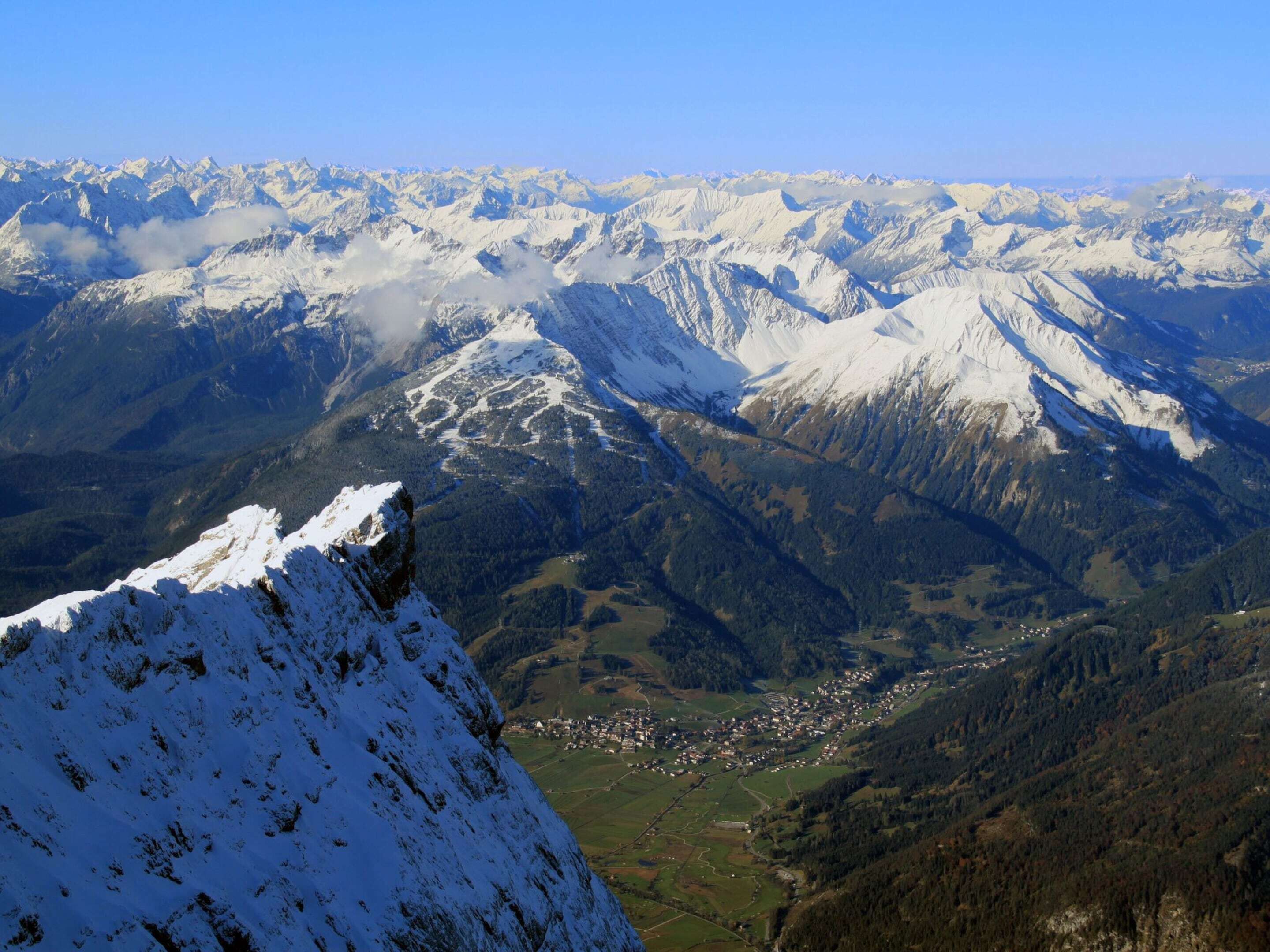 A mountainous landscape with snow-covered peaks and a valley with a small town.
