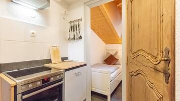 A compact kitchen with a stove, oven, and a small countertop. There is a bed with a wooden headboard in the adjacent room.