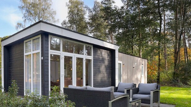 A modern, compact house with large windows, a patio with outdoor furniture, and a lush garden. - Chalet by Forest Edge With Modern Design (Markelo)