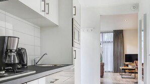 A modern kitchen with white cabinets and a black countertop, leading to a dining area with a TV and a table. - Chalet by Forest Edge With Modern Design (Markelo)