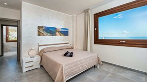 Een moderne slaapkamer met een bed, nachtkastje, raam met uitzicht op zee en een schilderij aan de muur.