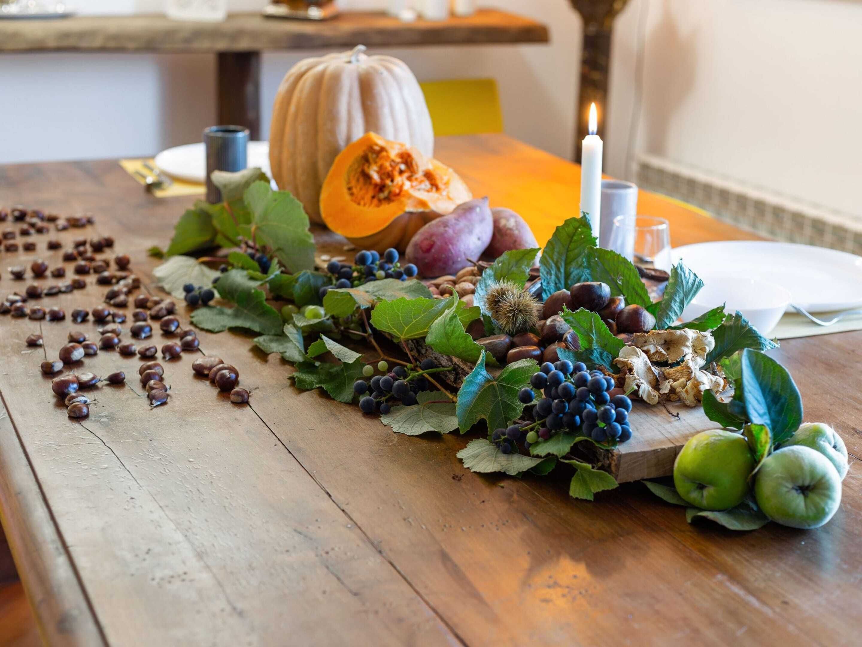 Une table en bois sur laquelle on voit une citrouille, des raisins, des châtaignes et des pommes.