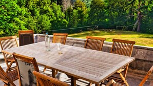 An outdoor dining area with a table and chairs, surrounded by lush greenery and a clear sky. - Castle With Wellness and Cinema (Gesves)