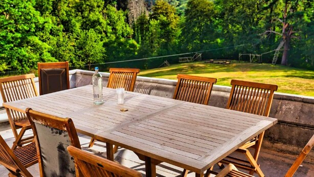 An outdoor dining area with a table and chairs, surrounded by lush greenery and a clear sky. - Castle With Wellness and Cinema (Gesves)