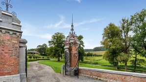 A gravel driveway leading to a gated entrance with a brick wall and decorative iron gate. - Castle With Wellness and Cinema (Gesves)