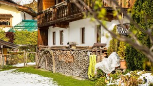 A traditional chalet with a stone wall, wooden balcony, and a garden with snow. - Chalet in Jochberg Near Thurn Pass (Jochberg)