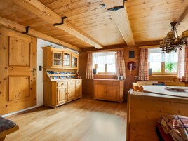 Ein Holzblockhaus-Interieur mit Küchenbereich, der Holzschränke, einen Esstisch und ein Fenster mit Vorhängen zeigt.