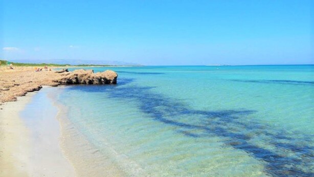 A beach with clear turquoise water, a rocky outcrop, and a sandy shore.